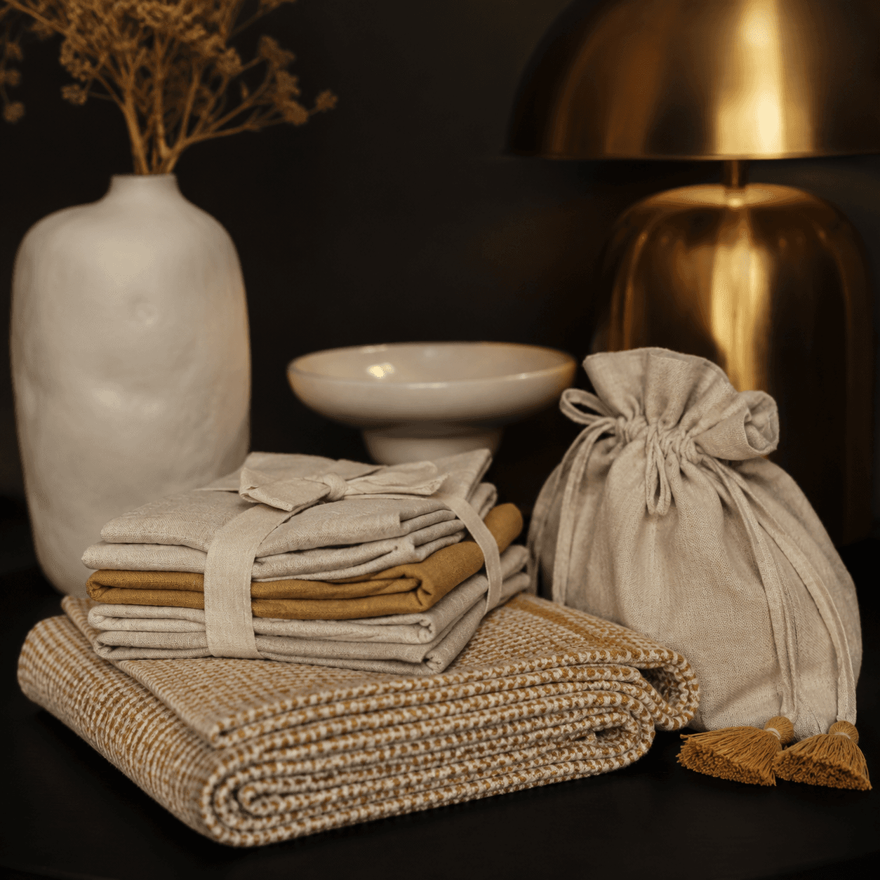 Stacked linen napkins, a folded throw and a cotton pouch in oatmeal and amber for cosy gifting.